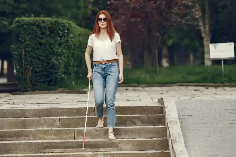 Mulher com deficiência visual descendo escadas com bengala, representando a aposentadoria da pessoa com deficiência